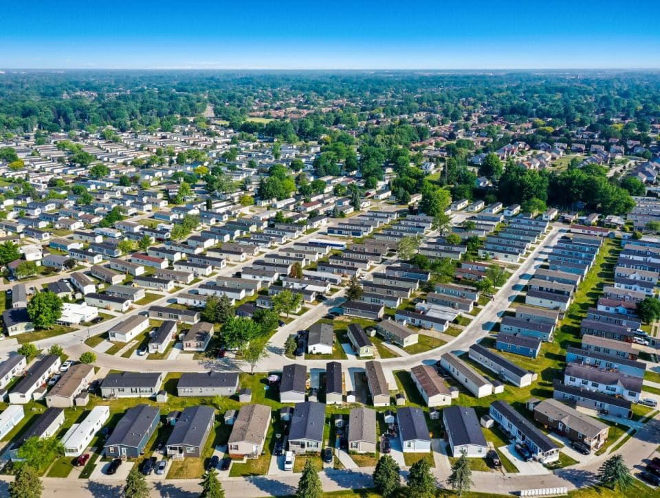 Aerial view of Rivers Edge, an all age MH community in Clinton Township, showcasing rows of houses, green trees, and neatly arranged streets under a clear blue sky.