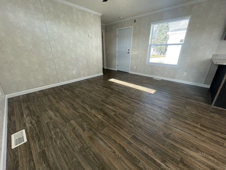 A bright, empty room with wood-look flooring, beige textured walls, a white front door, a window letting in sunlight, and white trim along the ceiling and baseboards.