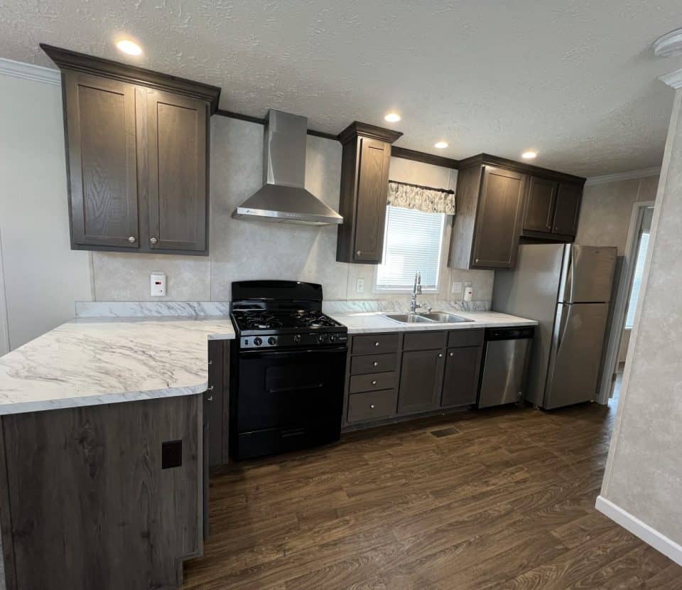 Modern kitchen with dark wood cabinets, marble countertops, stainless steel refrigerator, dishwasher, and range hood, black stove, double sink under a window, and wood-look flooring. Bright and clean appearance.
