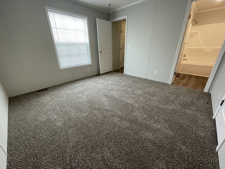 Empty bedroom with gray carpet, light gray walls, a window with blinds, white trim, open door to a closet, and an open doorway leading to a bathroom with a bathtub.