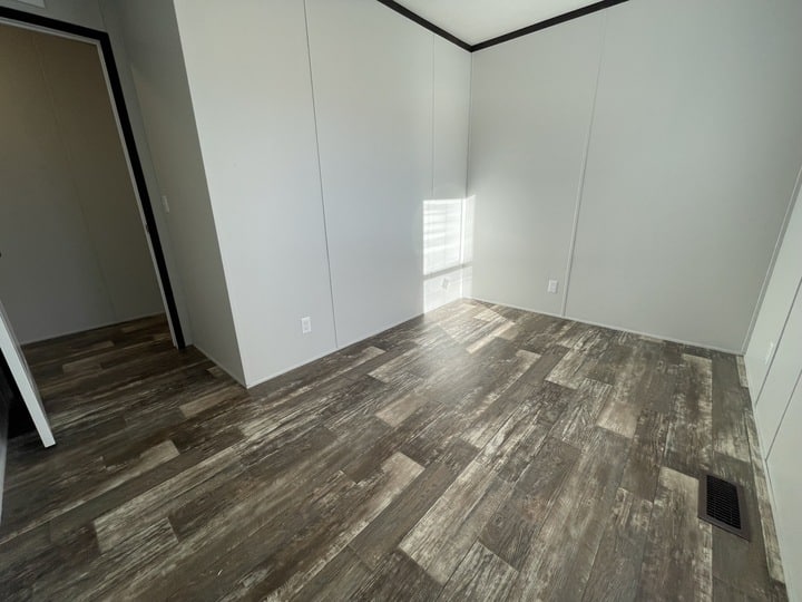 Empty room with light gray walls, dark trim, and wood-patterned vinyl flooring. Sunlight shines through a small window onto the floor. Two doorways are visible, one leading to another room.