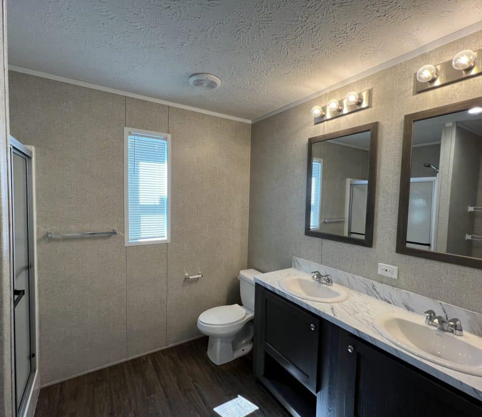 Modern bathroom with wood-look flooring, double sink vanity with marble countertop, two mirrors with lights, a toilet, a towel rack, a narrow window, and a shower with a glass door.