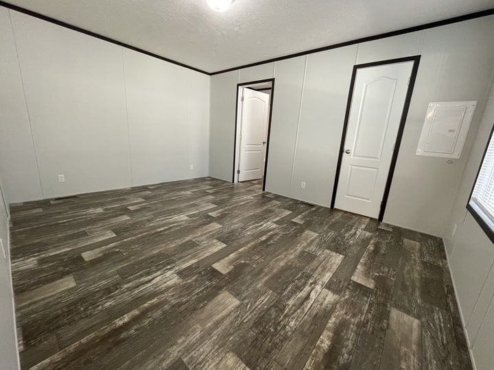 An empty room with wood-patterned vinyl flooring, light-colored walls, two white doors, a ceiling light, and a window on the right letting in natural light.