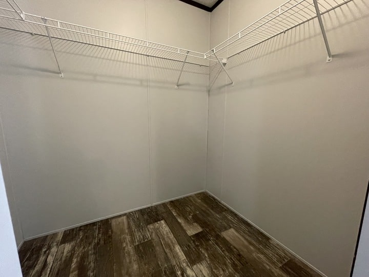 Empty walk-in closet with beige walls, wood-style flooring, and white wire shelves mounted along two adjacent walls near the ceiling.