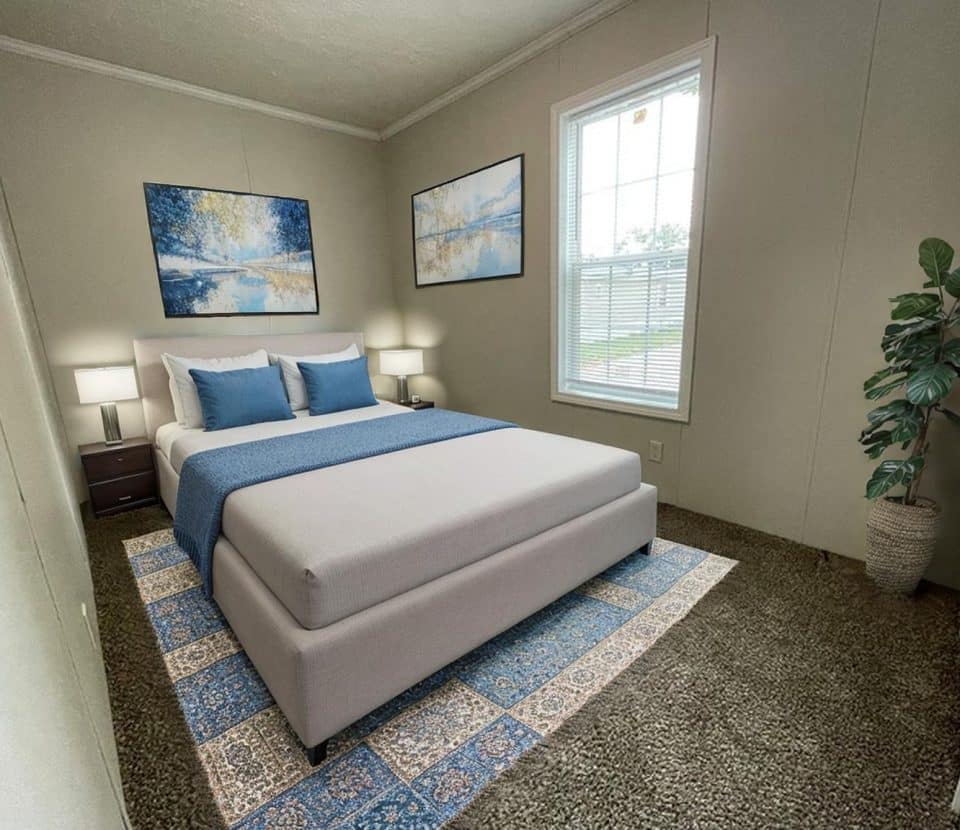 A cozy bedroom with a large bed, blue and white bedding, two nightstands with lamps, nature-themed wall art, a window with blinds, a potted plant, and a patterned rug on brown carpet.