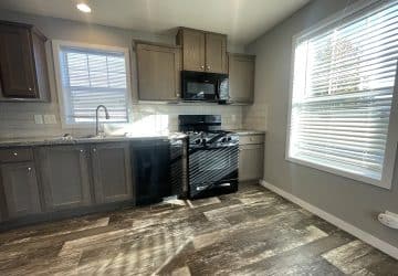 Modern kitchen with wood cabinets, a black stove and microwave, dishwasher, tiled backsplash, and large windows letting in natural light, with wood-look flooring.