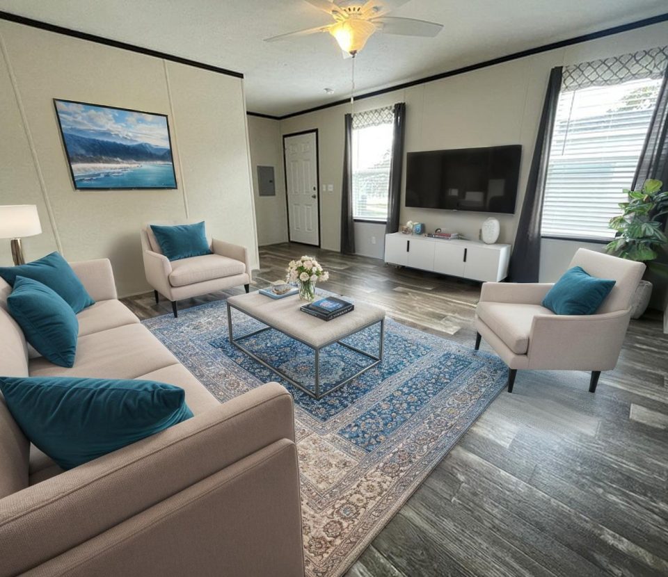 A modern living room with a beige sofa, two matching armchairs with teal pillows, a patterned blue rug, a coffee table, a flat-screen TV on the wall, large windows with curtains, and a potted plant in the corner.