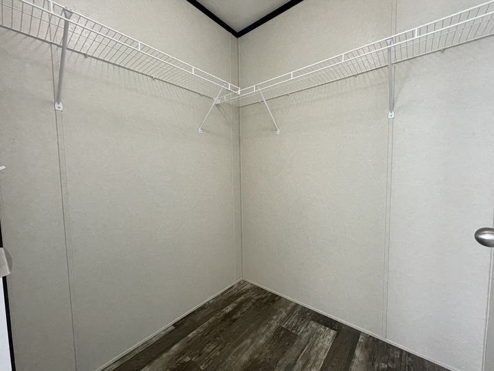 Empty walk-in closet with beige walls, dark wood-style flooring, and white wire shelves installed along two walls.