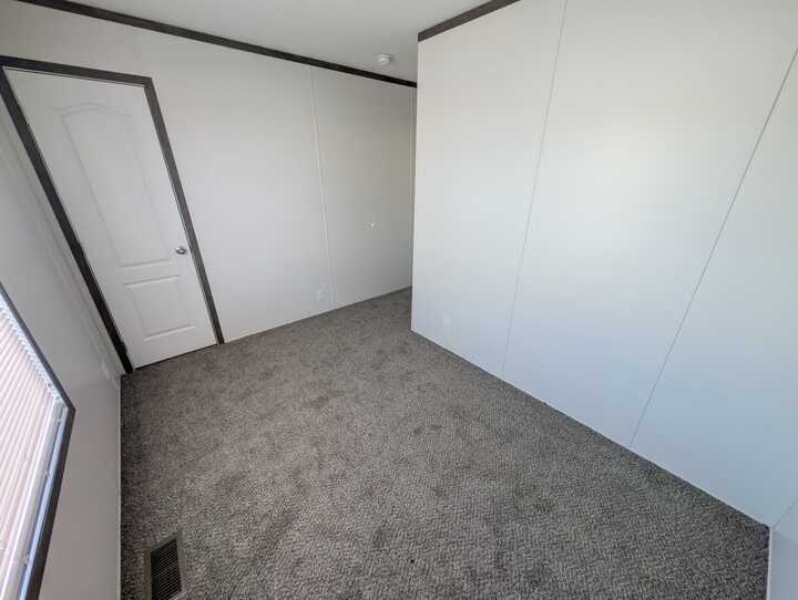 Empty room with light gray carpet, white walls, a closed door, and a window with blinds letting in natural light. The room appears clean, simple, and unfurnished.