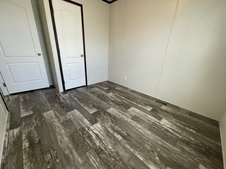 Small empty room with light-colored walls, wood-patterned vinyl flooring, and two white doors. The space is well-lit and unfurnished, showcasing a simple and clean interior.