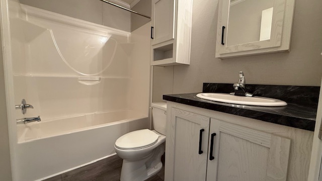 A small, modern bathroom with a white bathtub-shower combo, a toilet, and a white vanity with a black countertop, sink, and mirrored cabinet above. The floor has wood-like vinyl planks.