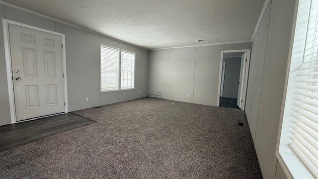 A spacious, empty living room with light gray walls, beige carpet, two large windows, and a white front door. A hallway leads to additional rooms, and natural light fills the space.