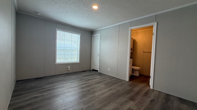 A bright, empty room with gray walls and dark wood flooring, featuring a large window, a closed closet door, and an open doorway leading to a bathroom with a visible toilet.