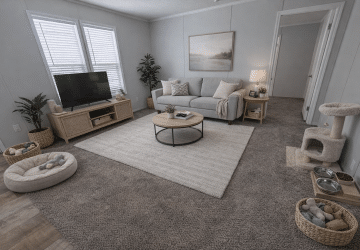A cozy living room with gray carpet, a light sofa, coffee table, TV on a stand, plants, a cat tree, pet bed, and pet bowls. Soft lighting and neutral colors create a warm, inviting atmosphere.
