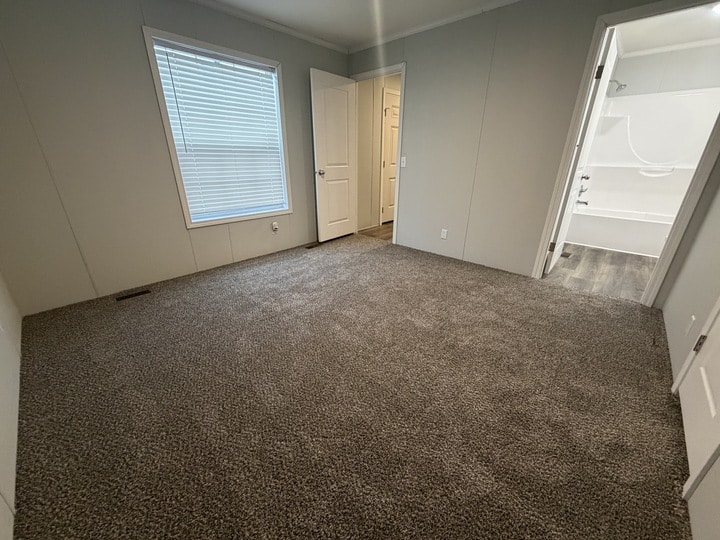 Carpeted room with light gray walls, a large window with blinds, an open closet door, and an open door leading to a bathroom with white fixtures and a bathtub.