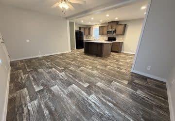 Open concept living area with gray wood-look tile flooring, beige walls, a ceiling fan, and a modern kitchen featuring dark wood cabinets, an island, black appliances, and recessed lighting.