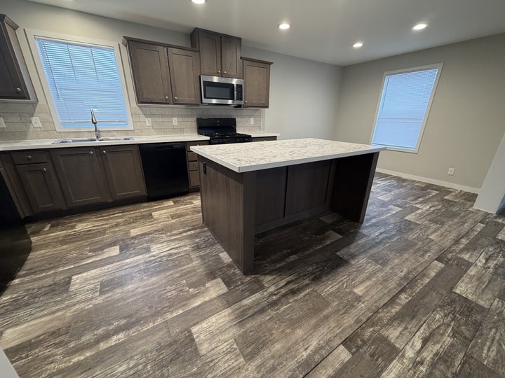 Modern kitchen with dark wood cabinets, a marble-topped island, stainless steel appliances, and wood-look flooring. Large windows provide natural light in the space.