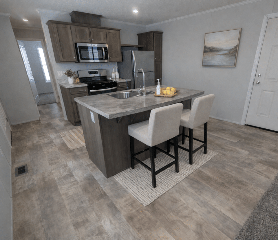 A modern kitchen with gray cabinets, stainless steel appliances, and a central island with two upholstered stools. The room has wood-look flooring, neutral walls, and a painting hung near a white door.