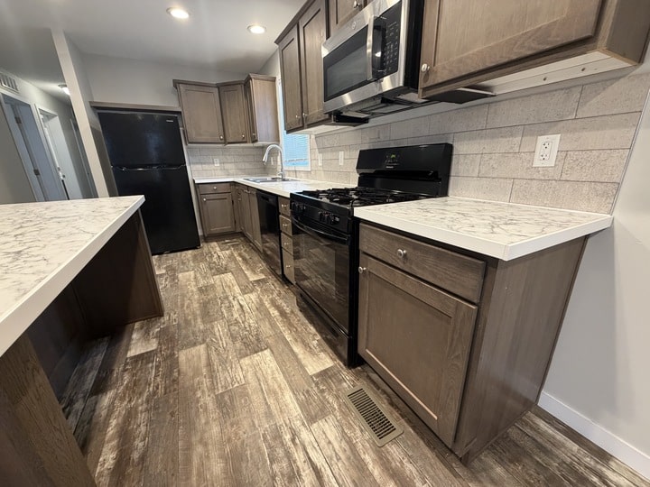 Modern kitchen with dark wood cabinets, white marble countertops, stainless steel appliances, black stove and refrigerator, wood-style flooring, and neutral tiled backsplash. Room is well-lit with recessed ceiling lights.