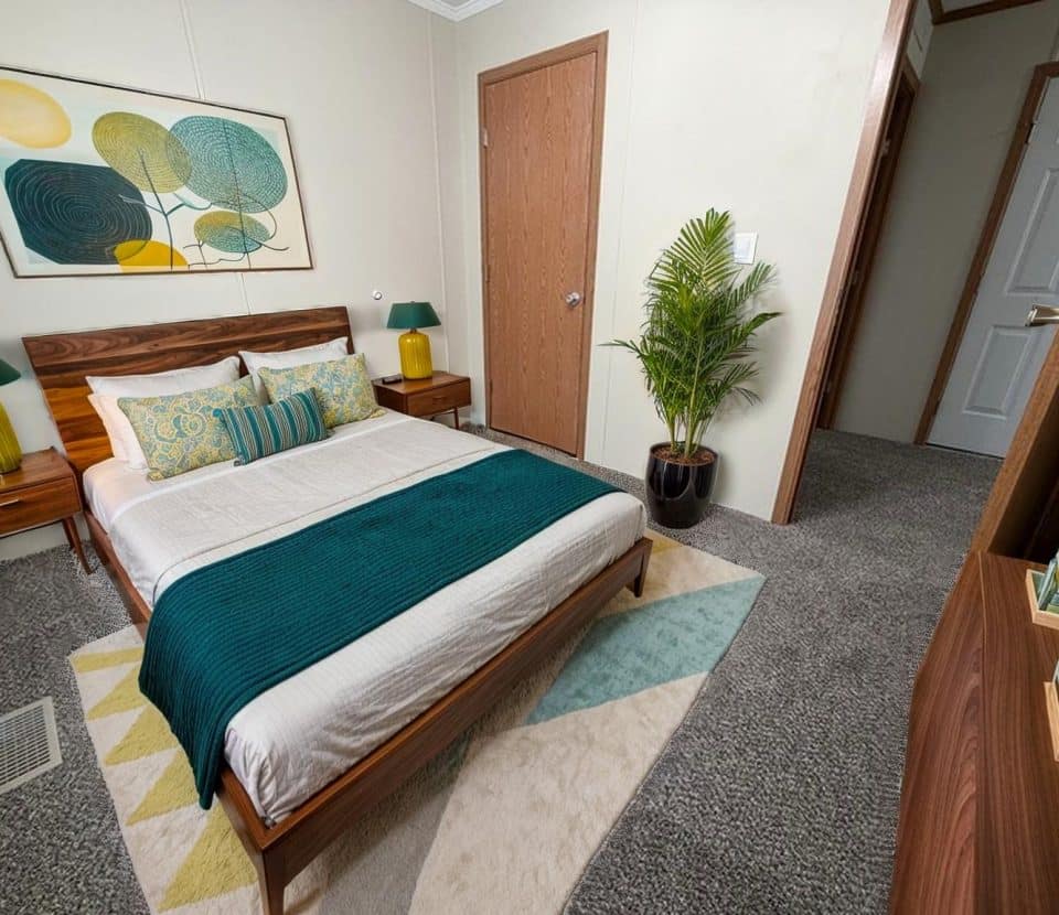 A modern bedroom with a wooden bed, teal and yellow bedding, two bedside tables with lamps, a potted plant, abstract wall art, and gray carpeted floor. A door and a dresser are also visible.