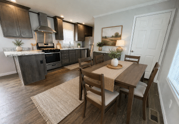 A modern kitchen and dining area with dark wood cabinets, stainless steel appliances, a dining table with six chairs, potted plants, neutral decor, and a landscape painting on the wall.