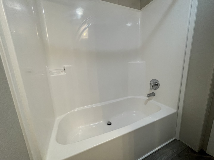 A clean, white bathtub-shower combo with a chrome faucet and a built-in soap dish, set against a smooth, white wall in a modern bathroom.