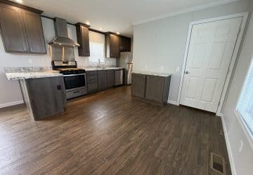 Modern kitchen with dark wood cabinets, stainless steel appliances, marble countertops, and a brown wood floor. A white door and window are on the right side; the space is well-lit with recessed lighting.