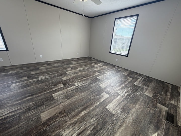 Empty room with light-colored walls, dark trim, wood-look vinyl flooring, two large windows letting in natural light, and a ceiling fan.