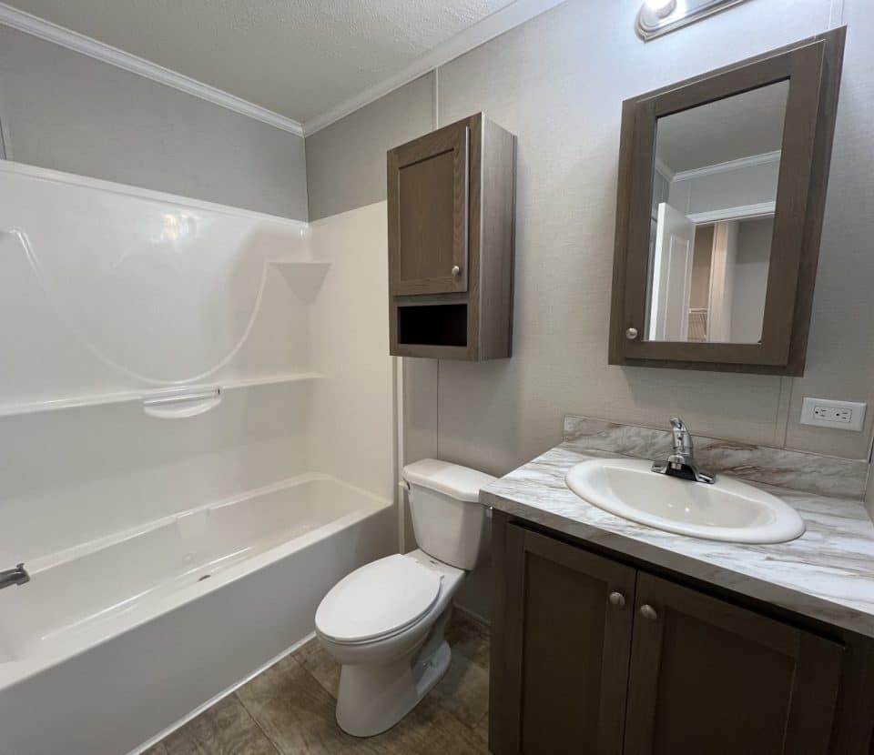 A small bathroom with a bathtub-shower combo, toilet, and a sink with a marble countertop. There are brown cabinets above the toilet and under the sink, and a mirrored medicine cabinet above the sink.