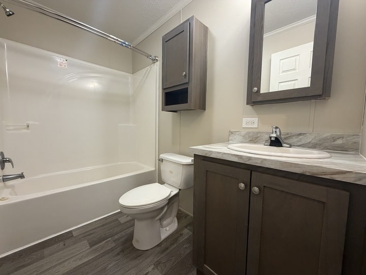 A modern bathroom with a bathtub and shower, toilet, and a vanity with a sink and mirror cabinet. The floor has gray wood-style tiles, and the cabinets are gray with silver handles.