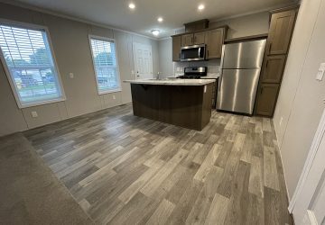 Modern kitchen with wood-look flooring, a center island, stainless steel appliances, and large windows letting in natural light. The space is open, bright, and unfurnished.