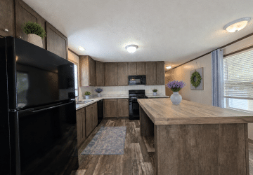 A modern kitchen with dark wood cabinets, a black refrigerator and stove, a large wood island, and decorative vases with purple flowers. Natural light streams through windows with blinds and light gray curtains.