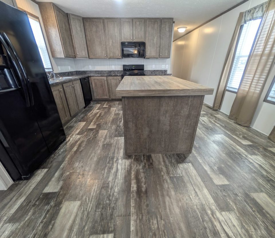 Modern kitchen with wood cabinets, a central island, black appliances including a fridge, dishwasher, and oven, and large windows with beige curtains. The floor has a gray wood-like pattern.