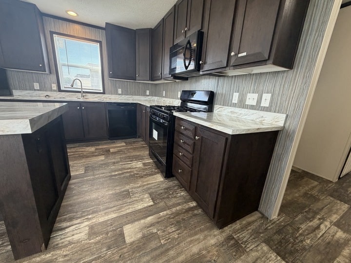 Modern kitchen with dark wood cabinets, marble-pattern countertops, stainless steel oven and microwave, dishwasher, and a window above the sink. The floor has a rustic wood-look finish.