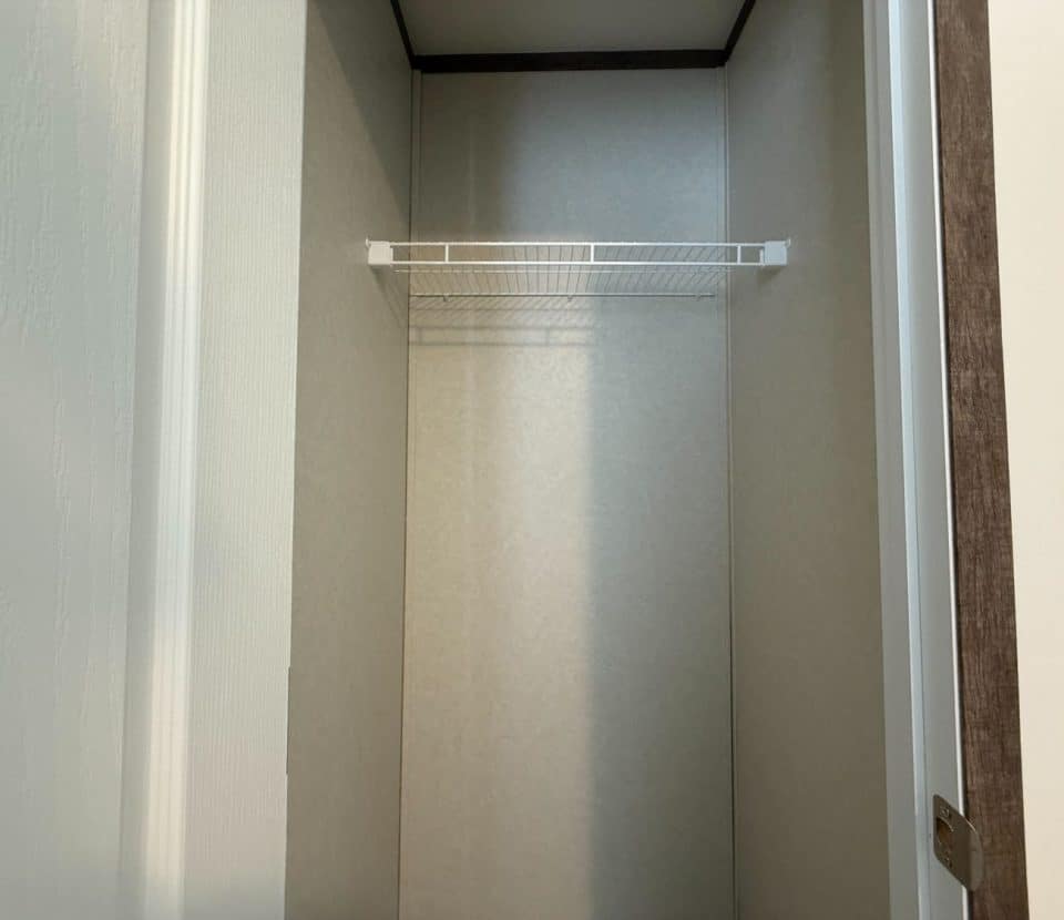 An empty closet with light-colored walls, a white door partially open, and a single white wire shelf installed near the top.