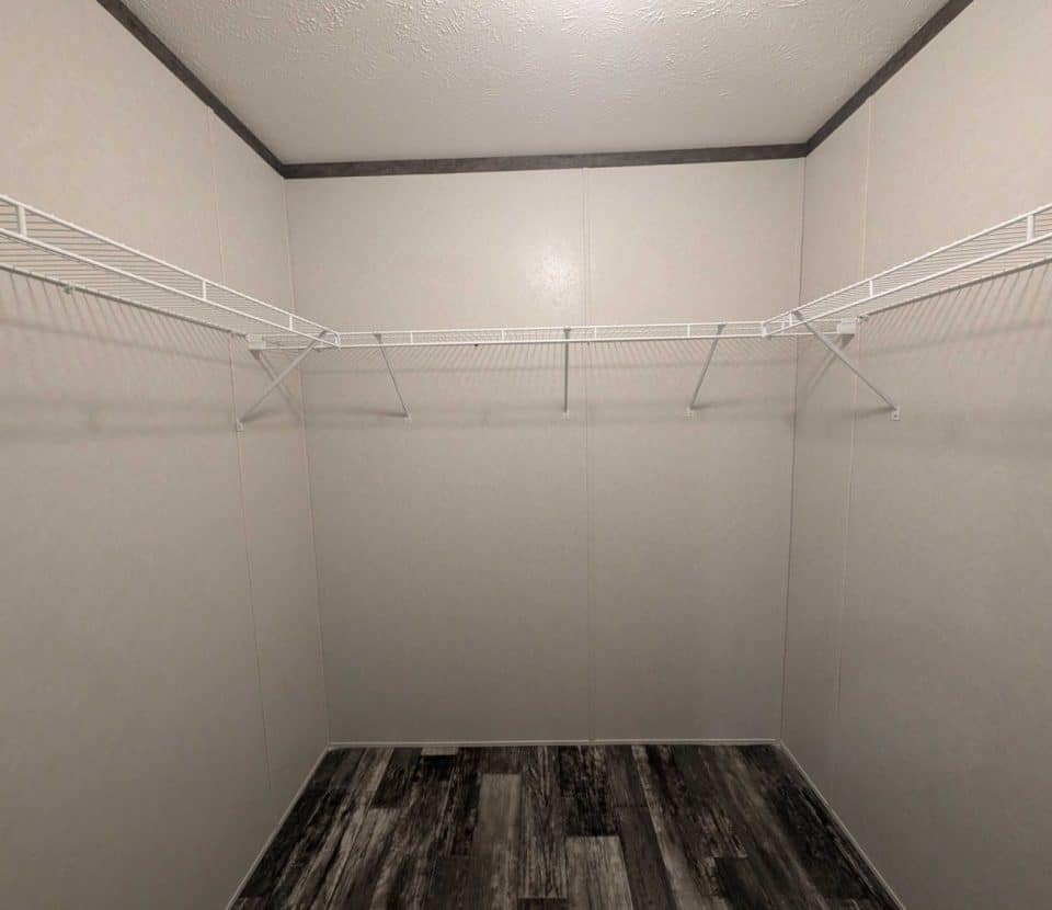 Empty walk-in closet with light-colored walls, white wire shelving units along two sides, and a dark wood-patterned floor. The ceiling is white with a textured finish.