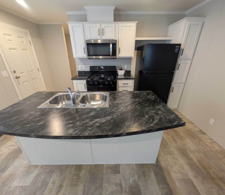 Modern kitchen with marble-look island countertop, stainless steel sink, white cabinets, black refrigerator, gas stove, microwave, and wood-look flooring. The space is clean and well-lit.
