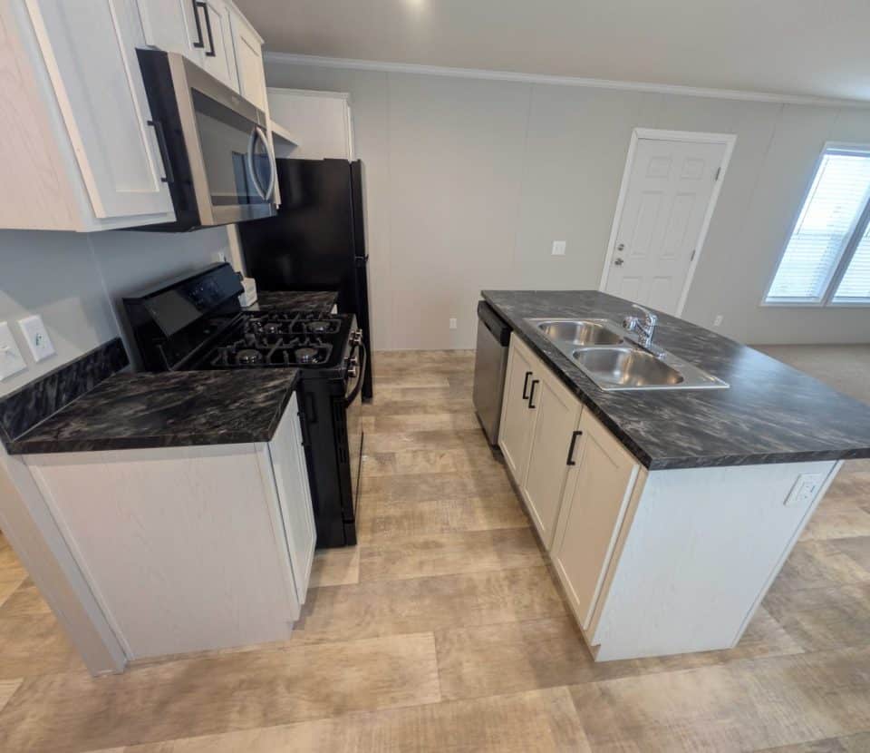 Modern kitchen with black appliances, marbled countertops, an island with a dual sink, light-colored cabinets, and wood-patterned flooring. A door and large windows with blinds are visible in the background.