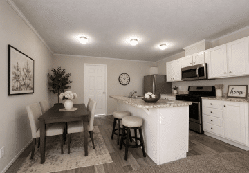 Modern kitchen and dining area with white cabinets, stainless steel appliances, a dining table for four with flowers, a kitchen island with two stools, wall art, a clock, and neutral-toned decor.