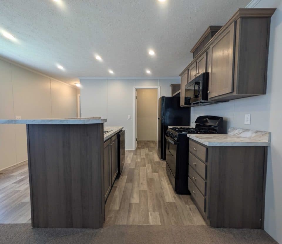 Modern kitchen with dark wood cabinets, marble countertops, gas stove, black refrigerator, microwave, and light wood flooring. Recessed ceiling lights brighten the space. A door and window are visible in the background.