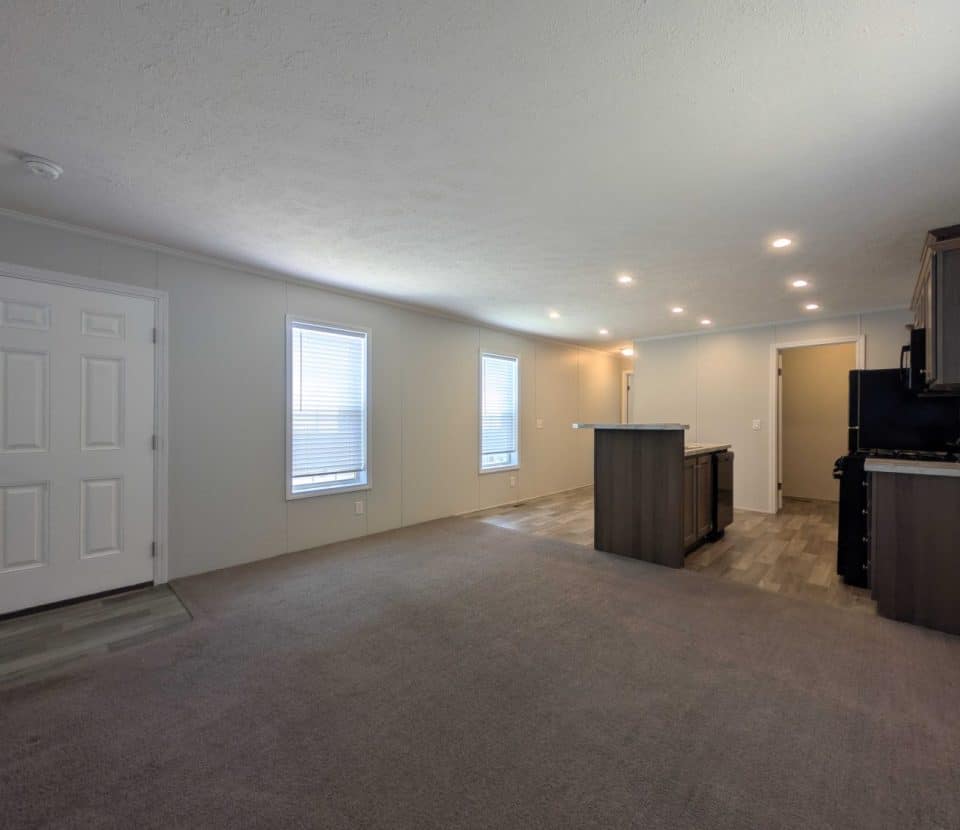 Open concept living room and kitchen with gray carpet, wood flooring in the kitchen, white walls, recessed lighting, and large windows bringing in natural light.